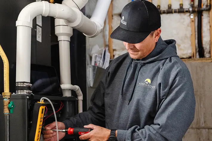 HVAC technician using a hand tool on furnace piping in a home mechanical room
